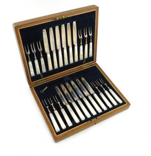 A set of twelve Edwardian silver fruit knives and forks, by The Goldsmiths and Silversmiths Company, London 1906, the blade with an engraved border, tapering mother-of-pearl handles, in a fitted wooden case.
