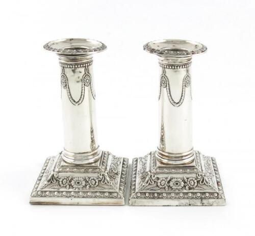 A pair of late-Victorian silver dwarf candlesticks, by Thomas Bradbury, London 1899, the columns with medallion and swag decoration, on raised square bases with foliate decoration, height 12cm. (2)