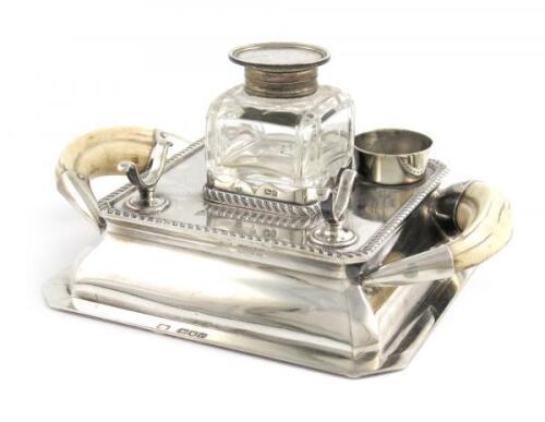 A late-Victorian silver and wild boar tusk inkwell, by Heath and Middleton, London 1900, square form, gadroon borders, tusk side handles, with a later silver-mounted inkwell, London 1907, length 21cm, approx. weight 15oz.