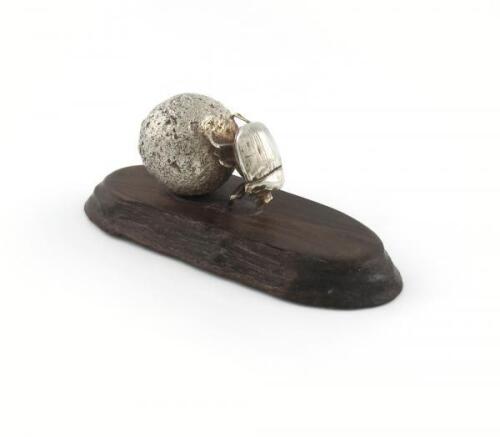 By Patrick Mavros, a Zimbabwean silver model of dung beetle at work, with his initials and Zimbabwean hallmarks, modelled pushing a ball of dung, on a wooden stand, total length a swimming position, length 18cm.